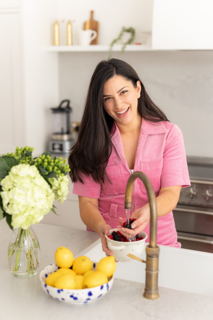 Natal nutrition coach washing fruit while laughing in a light-filled kitchen in Chiswick, London.